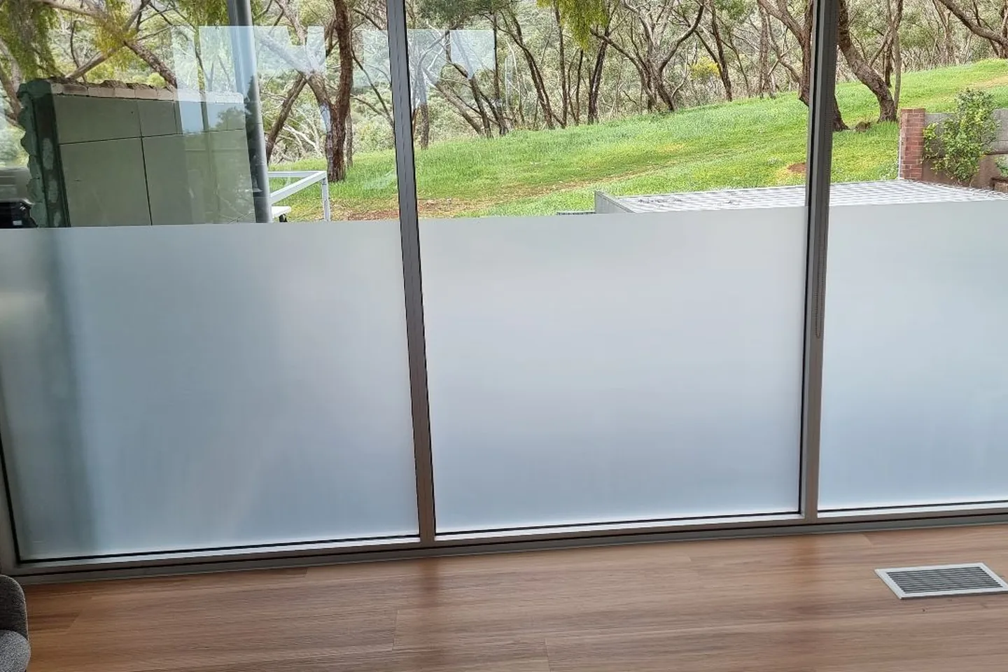 Floor-to-ceiling glass in a living area with a frosted film band across the lower panes and the garden visible above