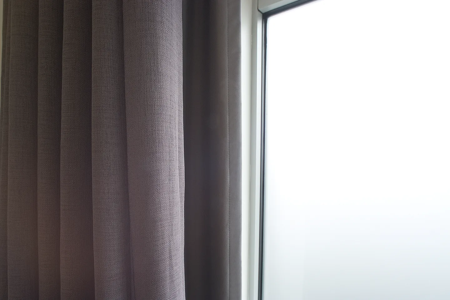 Close view of frosted film on a window pane beside the folds of a charcoal curtain