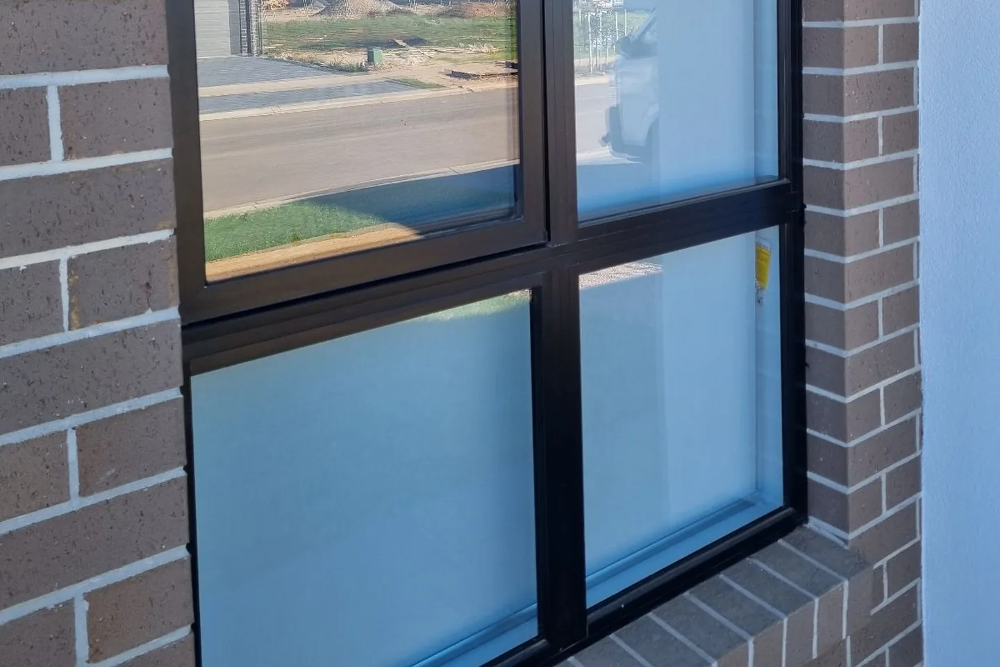 Black-framed window in a brick wall with frosted film on the lower panes and clear glass above