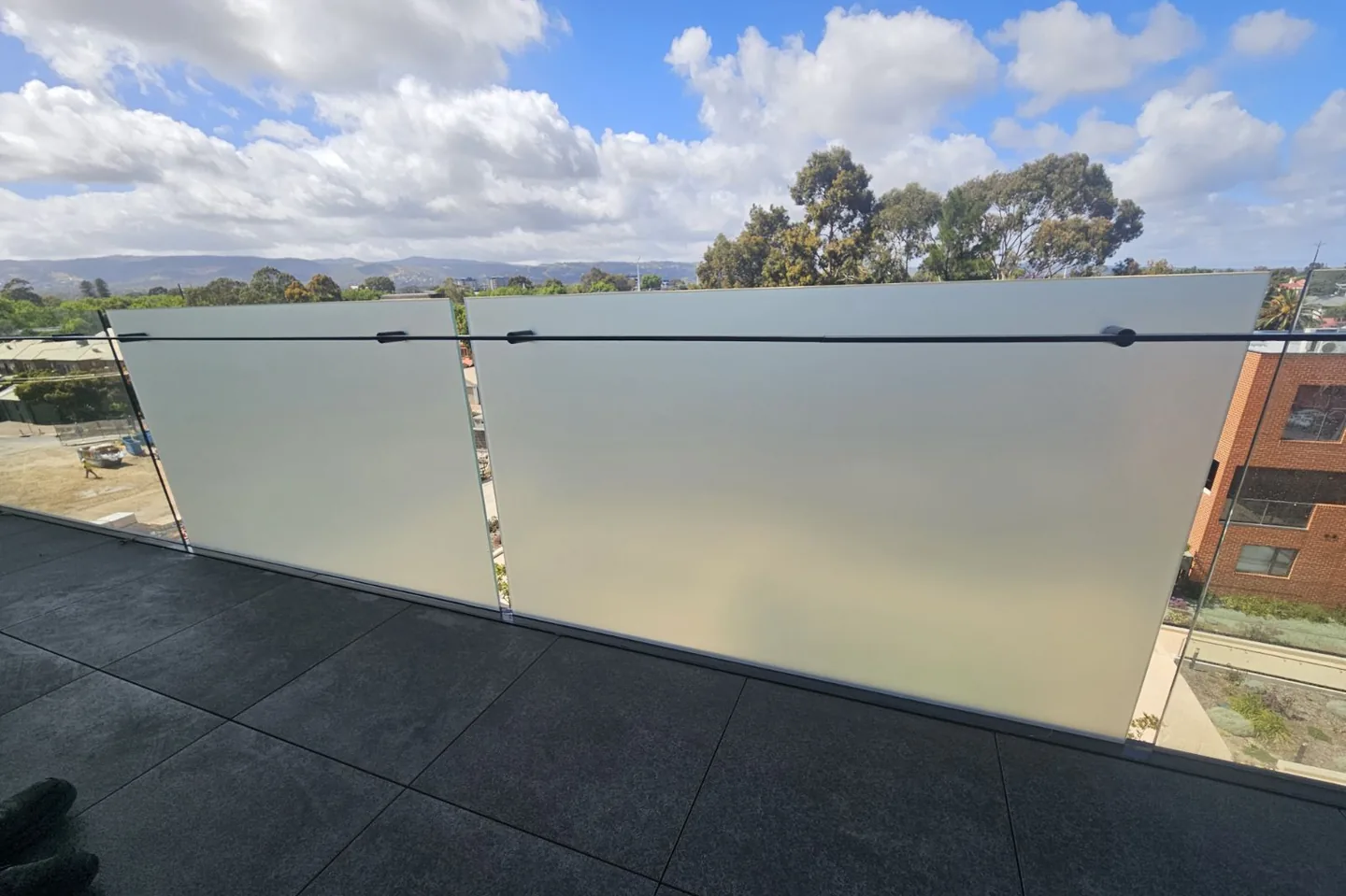 Glass balcony balustrade with frosted film applied, looking out over rooftops and trees