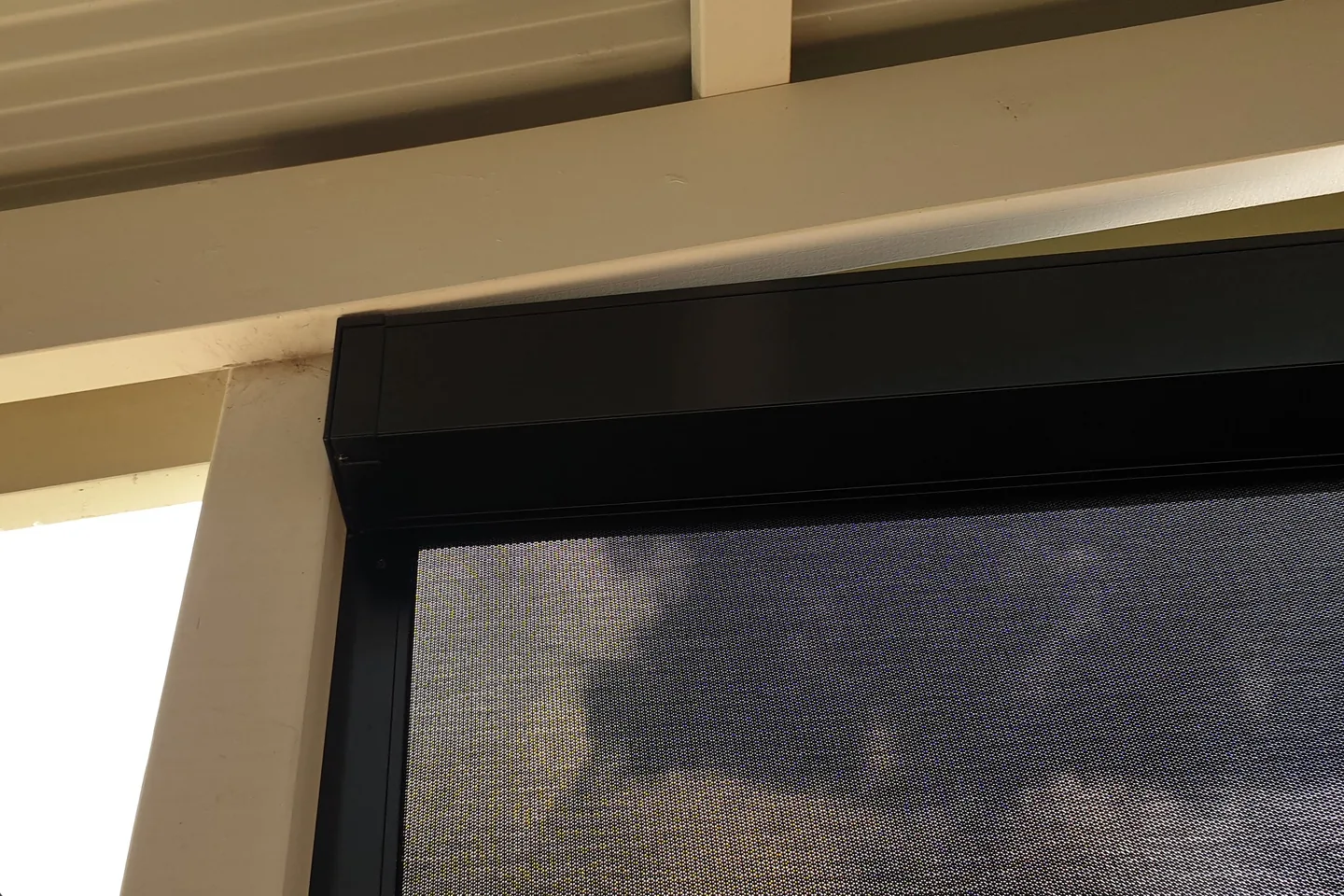 Black Zipscreen headbox and side channel meeting under a verandah beam, with the mesh blind lowered below