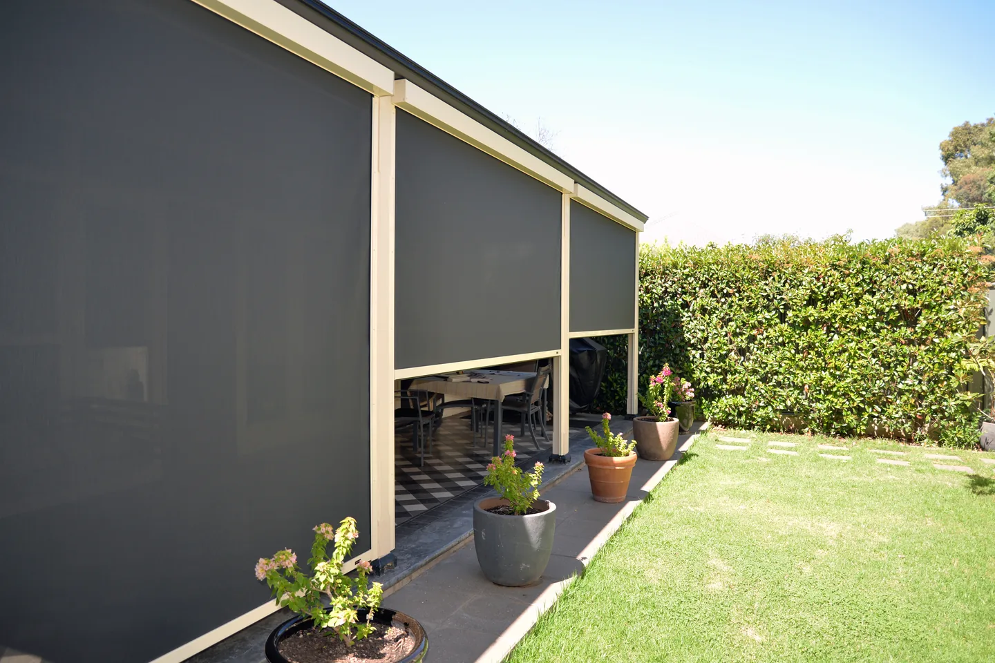 Row of lowered mesh outdoor blinds along a verandah beside a lawn