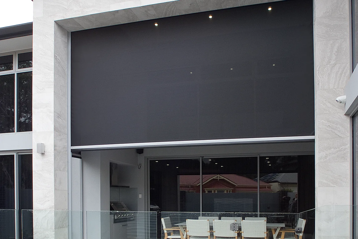 Large outdoor blind part-lowered across a two-storey opening behind a swimming pool