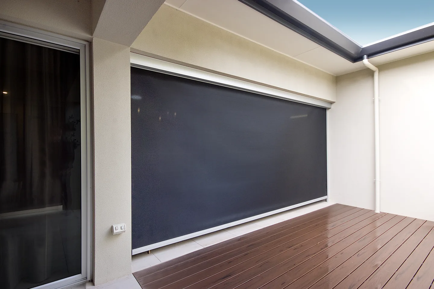Alfresco opening beside a timber deck with a dark mesh outdoor blind fully lowered