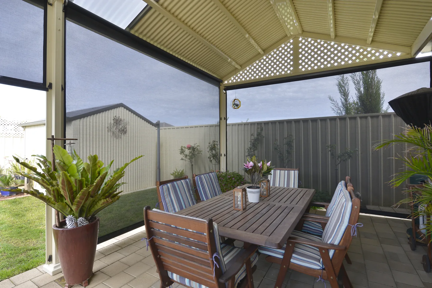 Outdoor dining setting under a gabled pergola with mesh outdoor blinds lowered on the open sides