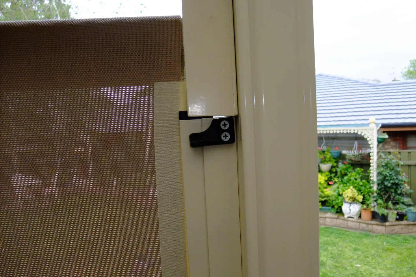 Ziptrak side track fixed to a cream pergola post, with the mesh blind and a black track bracket beside it